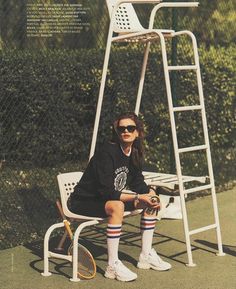 a woman sitting on top of a white chair next to a tennis racquet