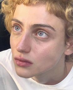 a close up of a person wearing a white shirt and looking at the camera with blue eyes