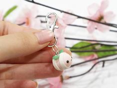 a hand holding a tiny keychain with a white and green bird on it