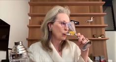 an older woman drinking from a wine glass in her living room with birds on the shelves behind her