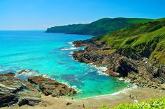 people are walking on the beach next to the blue water and green hills in the background