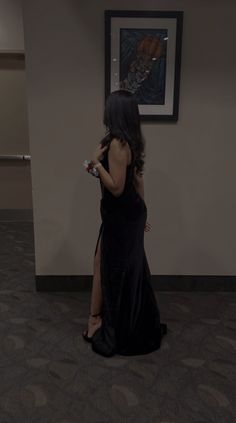 a woman in a long black dress is holding a video game controller and looking at the wall