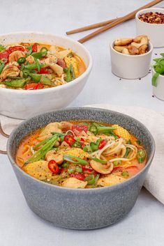 two bowls of food on a table with chopsticks and spoons next to them