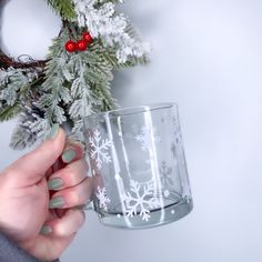 a woman holding a glass with snowflakes on it and a christmas wreath in the background