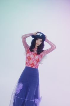 a woman in a skirt and hat poses for the camera with her hands behind her head