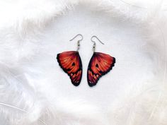 a pair of orange and black butterfly shaped earrings on white furnishing with feathers in the background