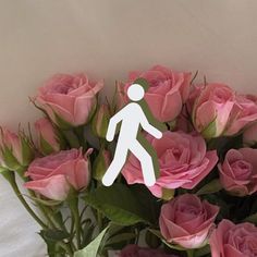 a vase filled with pink roses next to a white paper cutout man walking over it