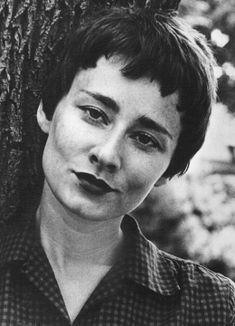 an old black and white photo of a young woman leaning against a tree with her tongue out