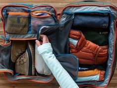 an open suitcase filled with clothes on top of a wooden floor next to a person's hand