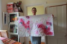 a woman holding up a large piece of paper with pink and blue paint on it