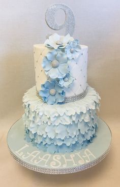 a three tiered blue and white cake with flowers on the top is decorated with silver icing