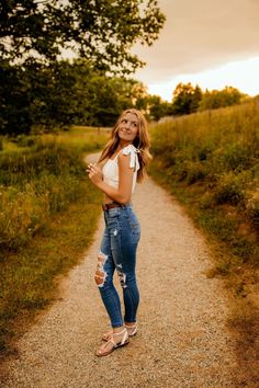 a woman standing in the middle of a dirt road with her hand on her hip