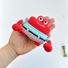 a hand holding a crocheted red and white stuffed animal