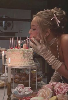 a woman blowing out candles on a cake with pink roses and other desserts around her