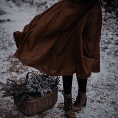 a woman standing next to a basket filled with pine cones and fir trees in the snow