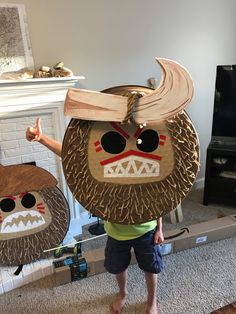 a person standing in front of a tv holding up two wooden masks with faces on them