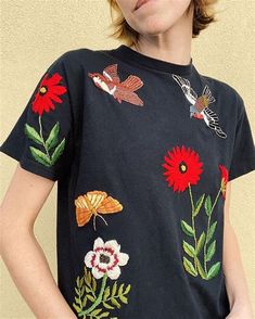 a woman wearing a black t - shirt with embroidered flowers and butterflies on the front