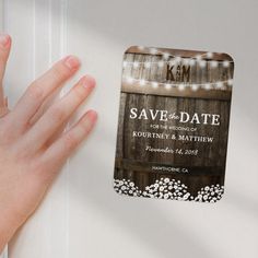 a hand is holding up a save the date card with string lights hanging from it