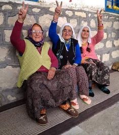 three women sitting on a bench with their hands in the air and one holding up two fingers