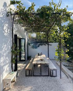 a wooden table sitting under a pergoline covered arbor next to a white building