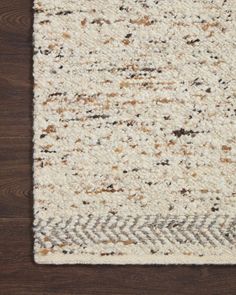 an area rug with brown and white colors on top of a wooden floor next to a wall