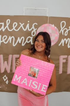 a woman is holding up a sign that says masie on it and wearing a pink dress