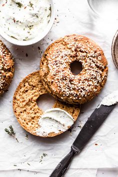 two bagels with cream cheese and herbs on them next to a bowl of dip