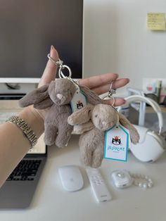 a person holding two stuffed animals in front of a laptop and keychain on a desk