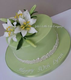 a green cake with white flowers and pearls on the top is sitting on a table