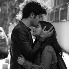 a young man and woman embracing each other on the street in front of a building