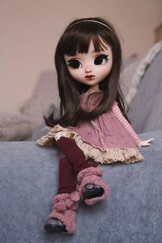 a doll sitting on top of a blue couch with her legs crossed and eyes wide open