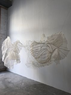 two white sculptures hanging from strings in an empty room