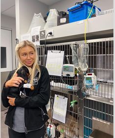 a woman is holding a small dog in a room filled with cages and medical equipment