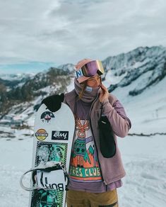 a person standing in the snow holding a snowboard and talking on a cell phone