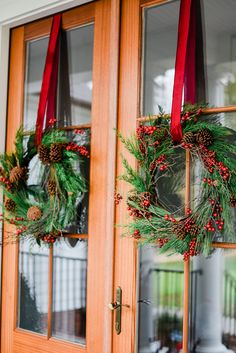 two wreaths hanging on the front door of a house with red ribbon and pine cones