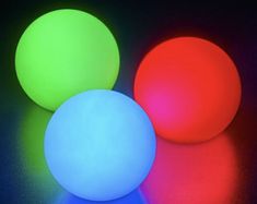 three glowing balls on a black surface with colored light coming from the top and bottom