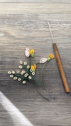 a wooden table topped with flowers and a sewing needle next to it on top of a piece of wood