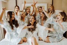 a group of women sitting on top of a bed in white robes and holding their hands up