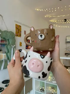 a person holding two mugs in front of a cow and bear face cup holder