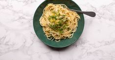 a green plate filled with pasta and parsley on top of a white marble table