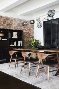 a dining room table and chairs in front of a brick wall with lights hanging from it