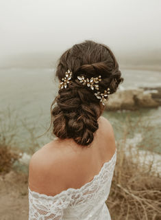 a woman wearing a white dress and gold hair comb looking out at the ocean on a foggy day