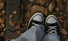 a person wearing black and white tennis shoes standing in leaves on the ground with their feet up