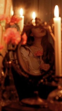 a reflection of a woman holding a flower in front of a mirror with candles behind it