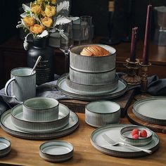 a table topped with plates and cups next to a vase filled with flowers on top of a wooden table