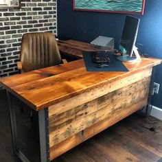 a wooden desk with a computer on it in front of a brick wall and wood floors