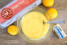 a glass bowl filled with yellow liquid next to two lemons and a carton of mayonnaise