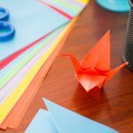 an origami bird sitting on top of a wooden table next to some papers