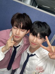 two young men posing for the camera in front of a blue wall with their fingers up