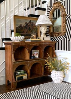 a wooden book shelf sitting under a stair case next to a painting on the wall